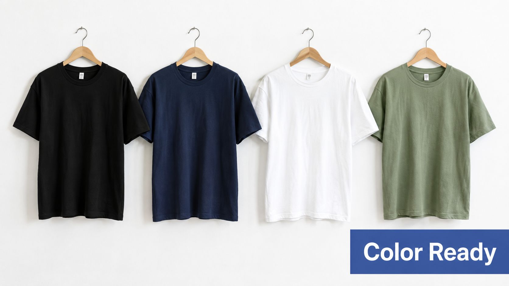 Four plain t-shirts in black, navy, white, and olive green hanging on wooden hangers against a wall.