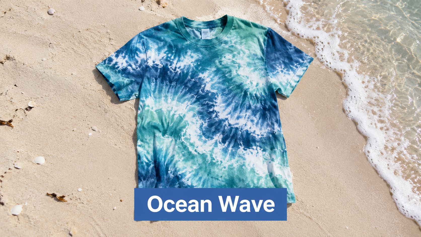 A blue and green tie-dye t-shirt laid out on sandy beach sand near the ocean water.