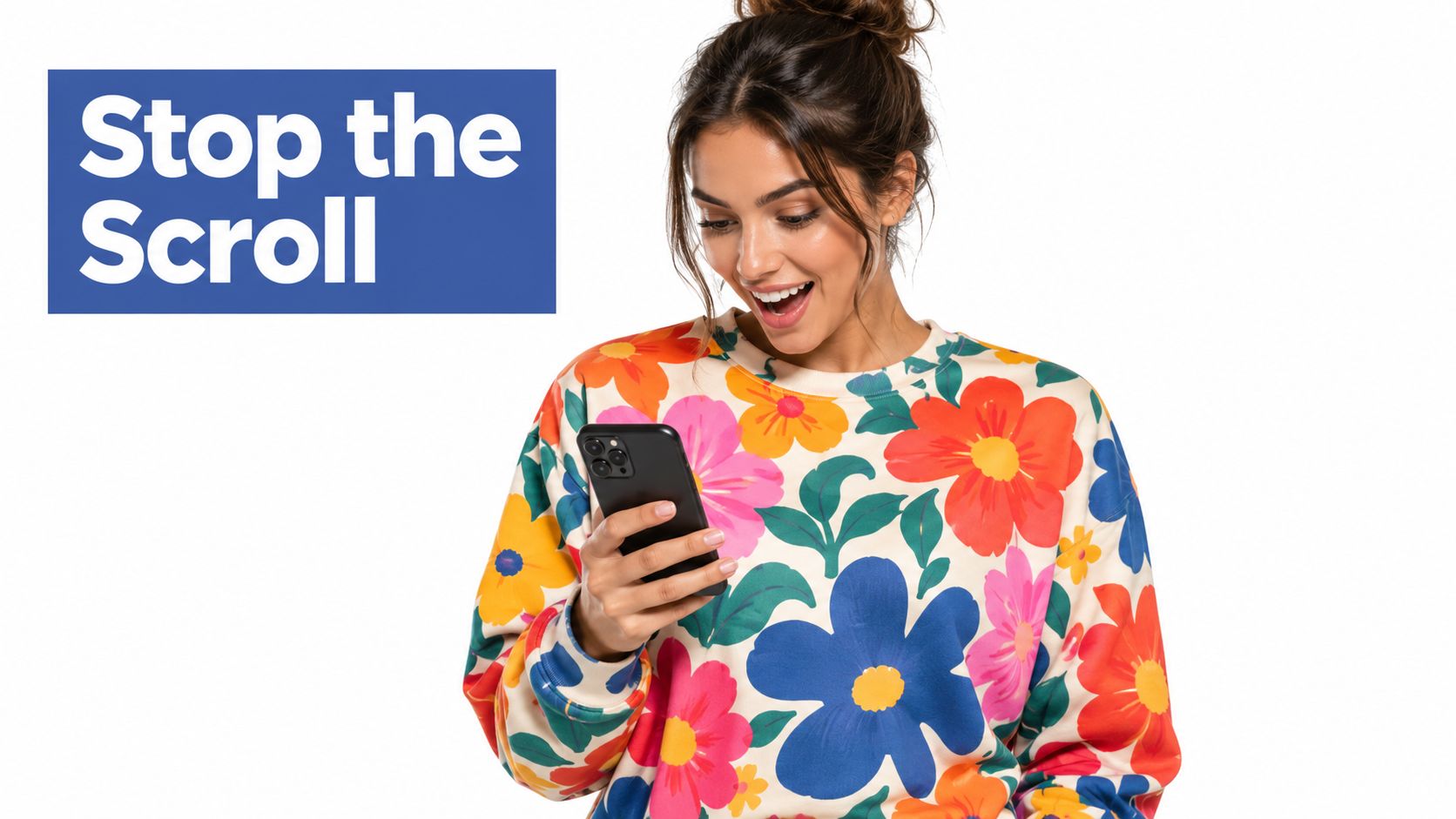 A smiling young woman wearing a vibrant floral patterned sweatshirt looking at her black smartphone screen.