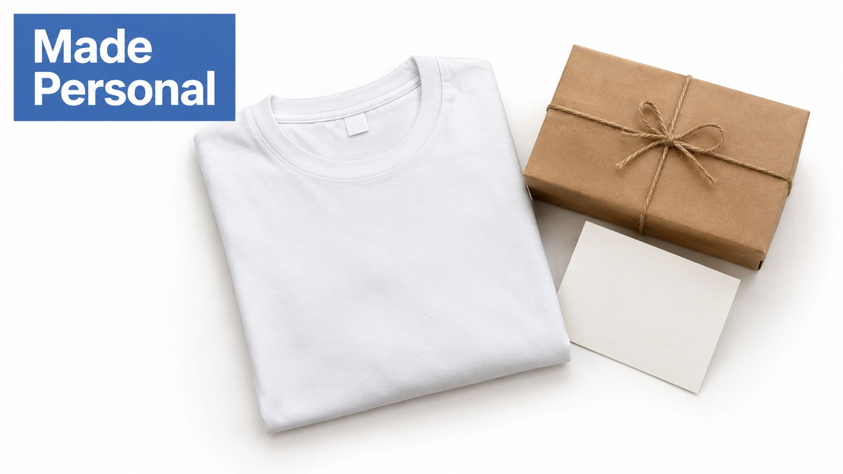 A white folded T-shirt sits beside a brown gift box wrapped with twine and a blank greeting card.